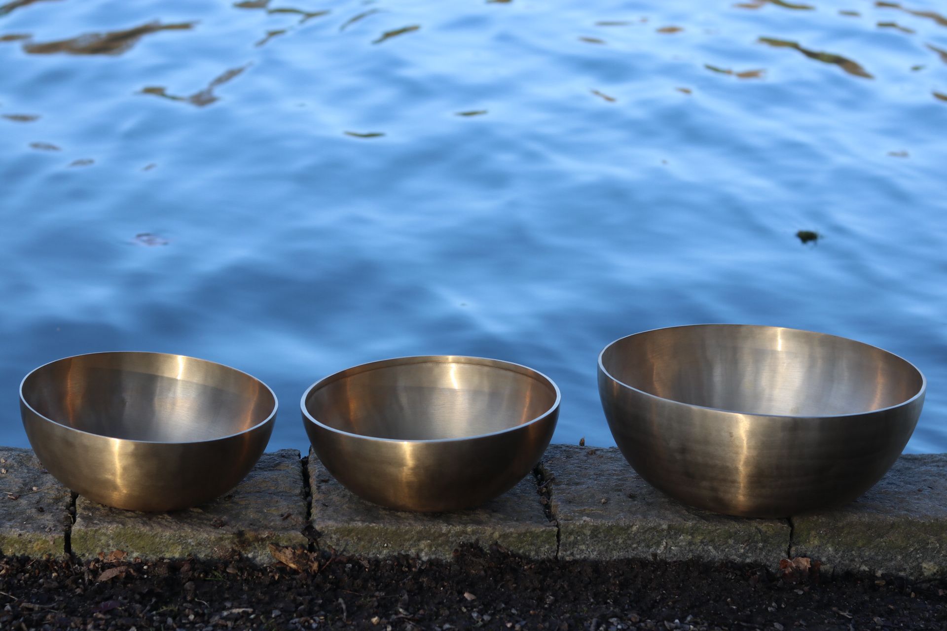 Drei goldene Klangschalen vor blauem Wasser